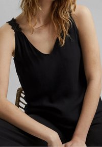 Top nero senza maniche con scollatura a V, caratterizzato da delicati dettagli in pizzo sulle spalle. Tessuto liscio, vestibilità rilassata e design minimale.