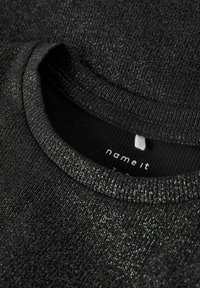 Sort strikket sweater med en struktureret, glitrende overflade. Har en rund halsudskæring og ribbede kanter. Brandmærket er synligt indeni.