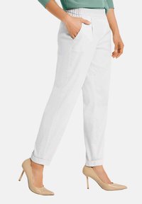 Witte broeken met een ontspannen pasvorm, voorzien van een gestructureerde tailleband met elastiek en zijzakken. Gecombineerd met beige hoge hakken.