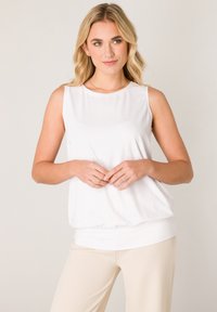 White sleeveless top with a round neckline, soft fabric, loose fit, and a gathered hem. Paired with light beige pants.