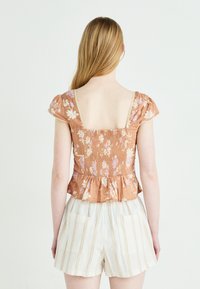 Brun blomstrete peplum topp med korte puffermer og smocket rygg. Har lyse lilla og hvite blomster, innfelt halskant, brukt med stripete shortser.