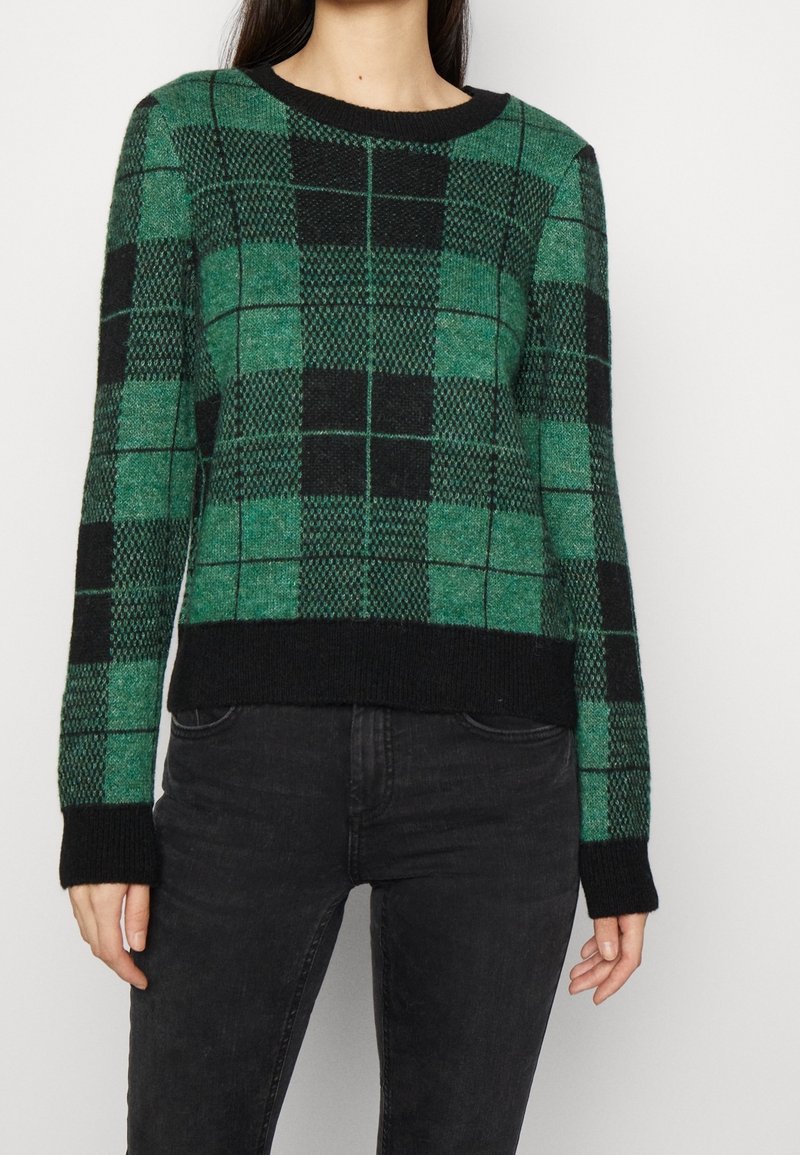 Pull à carreaux verts et noirs avec un col rond, des poignets et un ourlet côtelés. En tissu texturé. Accents noirs sur les bords.