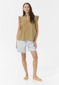 Top verde oliva texturizado con mangas rizadas y escote abotonado, combinado con pantalones cortos de mezclilla azul claro y chanclas amarillas.