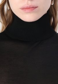 Svart turtleneck genser i et tynt, ribbestrikket stoff. Har høy krage og tettsittende design, med en jevn tekstur og subtil glans.