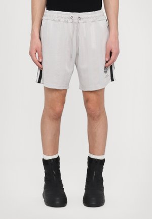 Lys grå shorts med elastisk liv og snøring. Har svarte side-striper og en liten logo på venstre lår. Brukt med svarte støvler.