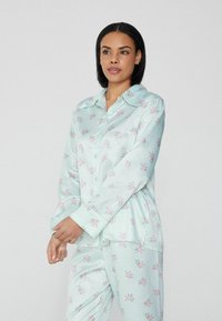 Hellgrünes Satin-Pyjama-Set mit pinkfarbener Blumenmusterung, langen Ärmeln, knöpfbarem Hemd und Hose mit elastischem Bund. Weicher Stoff mit Glanz.