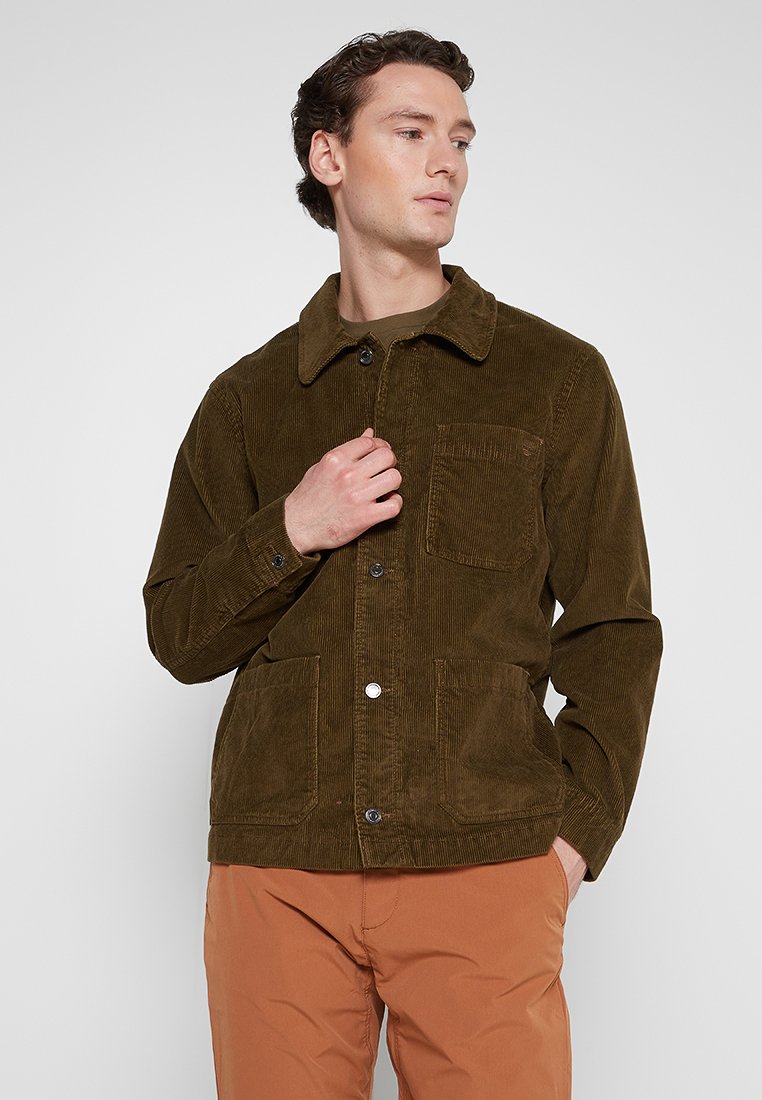 Brązowa kurtka z korduroy z kołnierzem, dwiema przednimi kieszeniami i zapięciem na guziki, wykonana z fakturowanej tkaniny i o prostym kroju.