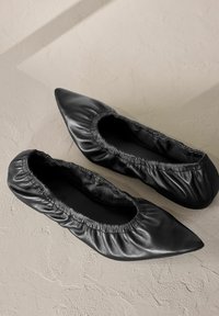 Schwarze Leder-Ballerinas mit einem gerafften elastischen Rand, spitzer Zehenform und glatter Textur. Entworfen für Komfort und Flexibilität in der Passform.