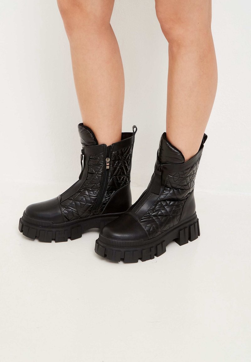 Botines negros hasta el tobillo con un patrón acolchado, fabricados con material similar al cuero, que cuentan con una suela gruesa y cremalleras laterales para facilitar su uso.