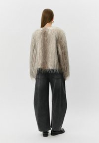 Puffasti, svijetlosivi pulover s teksturiranim, prugastim uzorkom; širokog kroja, s resicama na rubu, u kombinaciji s širokim crnim trapericama i crnim cipelama.