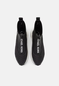 Černé slip-on tenisky s texturovaným textilním svrškem, bílým logem a kontrastní gumovou podešví. Disponují hladkým zipovým uzávěrem.