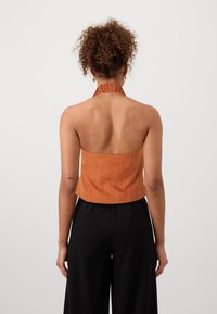 Πορτοκαλί τοπ με λουράκι φτιαγμένο από υφασμάτινη υφή, με εφαρμοστό μπούστο και ανοιχτή πλάτη. Συνδυάζεται με μαύρο παντελόνι σε φαρδιά γραμμή.