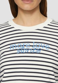 Gestreepte katoenen t-shirt met marineblauwe en witte horizontale strepen. Heeft blauwe geborduurde tekst "more love stories" op de borst.