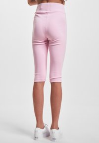 Rosa bomull leggings med en tettsittende design, midt på leggen lengde, og et bredt midjebånd, kombinert med hvite joggesko. Glatt tekstur, ingen synlige mønstre.