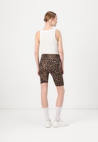 Bijela majica bez rukava u kombinaciji s biciklističkim šortsem s leopard uzorkom u crnoj i bež boji. Model nosi bijele čarape do gležnjeva i bijele tenisice.