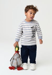 Striped gray and white long-sleeve shirt with duck graphic, paired with navy blue cargo pants and white sneakers, holding a plush duck toy.