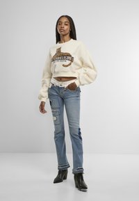 Sudadera corta de color crema con detalles de estampado de leopardo, combinada con jeans de color azul claro que presentan parches y dobladillos deshilachados. Botines negros de tacón.