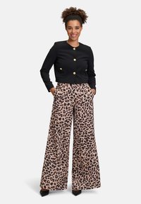 Veste noire courte avec des boutons dorés, associée à un pantalon à jambes larges en beige avec un imprimé léopard noir, doté de poches et d'un tissu lisse.
