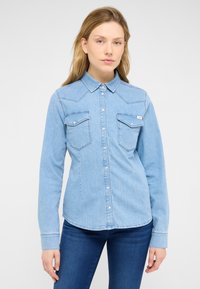 Heledsinine teksashirt pikkade varrukatega, terava kraega ja nööpidega eest. Kaks rinnataskut klappidega ja õmmeldud detailidega.