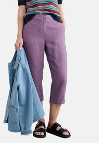 Lila lanena kratka hlače z gumbom in stranskimi žepi, kombinirane s svetlo modrim denim jopičem in črnimi sandali.