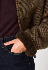 Giacca in misto lana a quadri marrone con un morbido polsino in pelliccia sintetica marrone. Abbinata a un maglione viola scuro e jeans in denim scuro.