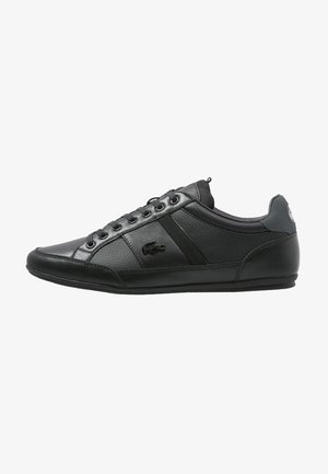 Zapatilla deportiva Lacoste negra de perfil bajo con paneles de cuero y malla, cordones delanteros y logo del cocodrilo en el lateral.