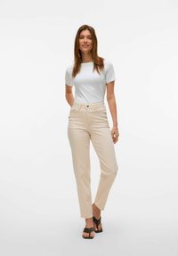 Hvit kortermet t-skjorte kombinert med lysebeige rette jeans. Modellen har på seg brune sandaler med stropper. Enkelt, rent design.