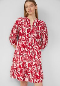 Rotes und weißes knielanges Kleid mit einem geometrischen und botanischen Muster, V-Ausschnitt, 3/4-Ärmeln und einem gerafften Taillenbereich.