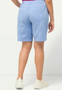 Světle modré bavlněné šortky s dvěma zadními kapsami, elastickým pasem a volným střihem, kombinované s bílými teniskami.