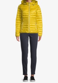 Gul puffjacka med huva, med vertikal quiltad design, dragkedjefickor och en smal passform, i kombination med marinblå byxor och svarta skor.