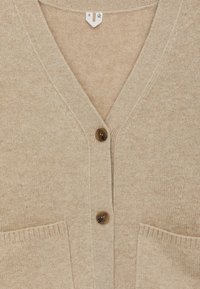 Beige Strickjacke mit V-Ausschnitt, zwei Fronttaschen und Knopfverschluss. Weiche Textur mit lockerer Passform.