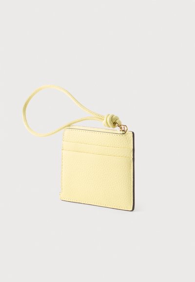 Petit porte-cartes en cuir jaune pâle avec poche avant et bracelet poignet boucle et noué à la fermeture éclair.