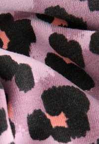 Stickad tyg i rosa med stora svarta och persikofärgade leopardmönster. Mjuk textur med en något fluffig utseende.