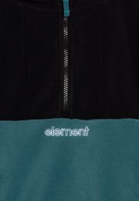 Fleecetröja med svart övre del och teal nederdel, med en framdragbar dragkedja och en broderad "element"-logotyp i vitt.