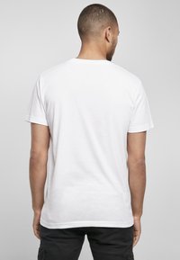 Weißes Baumwoll-T-Shirt mit Rundhalsausschnitt und kurzen Ärmeln, das eine glatte Textur aufweist. Figurbetontes Design mit geradem Saum am unteren Ende.