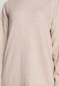 Beżowy sweter dziany o miękkiej fakturze, z okrągłym dekoltem i opuszczonymi ramionami dla luźnego kroju.