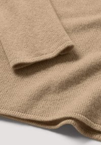 Beige gebreide trui met een gestructureerd oppervlak, voorzien van een brede manchette en een soepele, vloeiende zoom. Het materiaal lijkt zacht en warm.