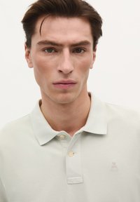 Hellgrünes Polo-Shirt mit strukturierter Oberfläche, ausgestattet mit einer zwei-knöpfigen Knopfleiste und einer dezenten Logo-Stickerei auf der linken Brust.