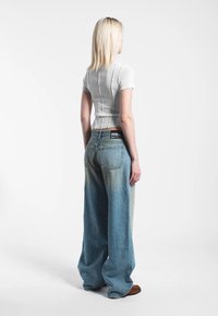 Vit ribbad croptop med korta ärmar kombinerad med ljusblå vida jeans med blekta partier och en mörkare midjeresår.