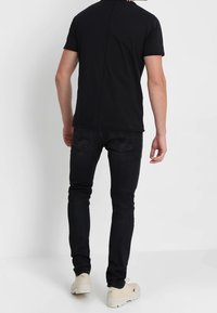 Sort t-shirt med korte ærmer og et rent design, parret med tætsiddende sorte jeans og beige fodtøj, der viser en enkel, moderne stil.