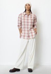 Plaid button-up shirt in soft fabric, featuring pale pink, cream, and beige colors. Paired with wide, light-colored trousers and dark boots.