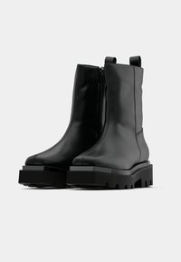 Μαύρα μποτάκια αστραγάλου από λείο δέρμα, με πλευρικό φερμουάρ, χοντρή σόλα πλατφόρμας και μινιμαλιστικό σχέδιο με στρογγυλεμένη μύτη.