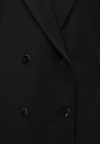 Manteau noir croisé à l'avant avec quatre boutons noirs brillants et un col à revers cranté large.
