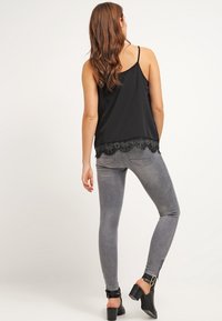 Camisola de satén negra con dobladillo de encaje, combinada con jeans ajustados gris claro y botas negras de tobillo con detalle de hebilla.