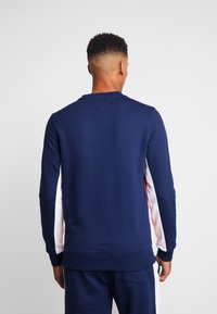 Mörkblå sweatshirt med långa ärmar och rundad hals, med vita och röda sidopaneler. Tillverkad av mjukt tyg med ribbade ärmslut.