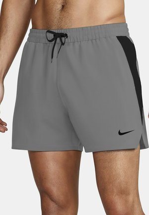 Uomo con pantaloncini sportivi grigi con pannelli laterali neri e logo Nike nero vicino all'orlo, vita elasticizzata con coulisse nera.