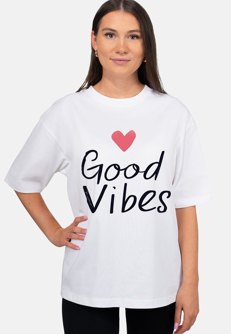 Witte oversized t-shirt met zwarte tekst "Good Vibes" en een roze hartontwerp. Korte mouwen en een losse pasvorm, gemaakt van zacht katoen.