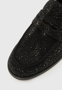 Mocassins noirs avec une surface texturée et scintillante composée de petites embellissements facettés. Présentent un bout lisse et arrondi ainsi qu'une bride décorative.