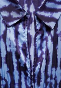 Blauwe en paarse tie-dye shirt met verticale strepen, voorzien van een kraaghalslijn en een zijdeachtige textuur. Geplooide stof zorgt voor visuele aantrekkingskracht.