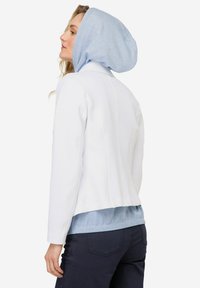 Chaleco blanco con un diseño ajustado y detalles de costura. Presenta una capucha a rayas azul claro, superpuesta a una parte superior texturizada azul.